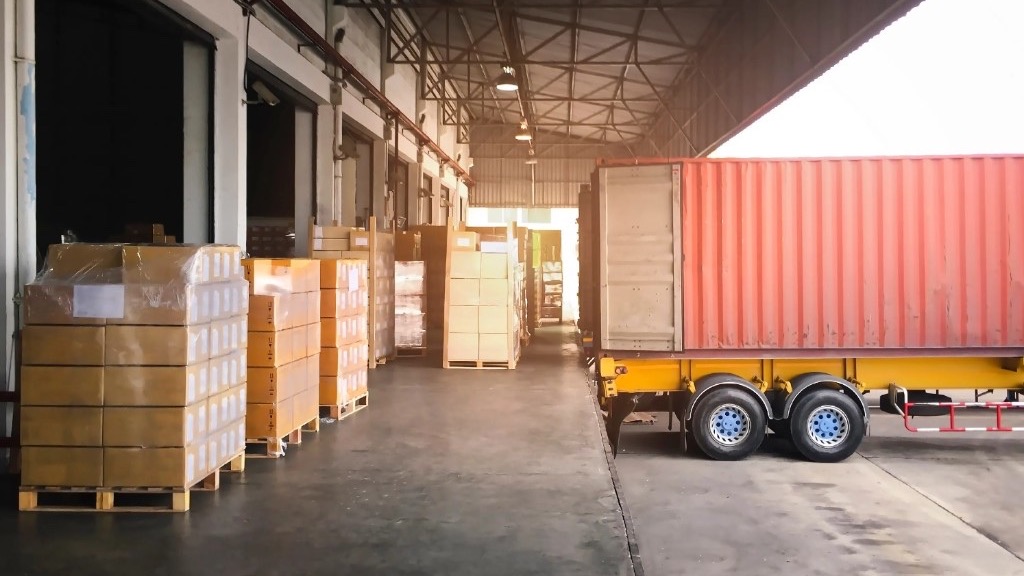 Andén de CEDIS con pallets encelofanados y contenedor rojo sobre tráiler amarillo