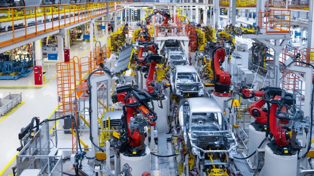 Línea de ensamble automotriz con robots rojos y carrocerías — flete y origen T-MEC