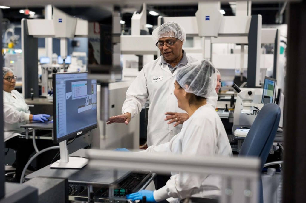 Quality control in a medical-device plant: metrology and station review with staff in lab coats